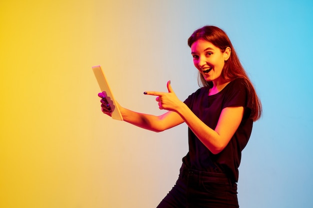 Young caucasian woman's portrait on gradient blue-yellow studio background in neon light