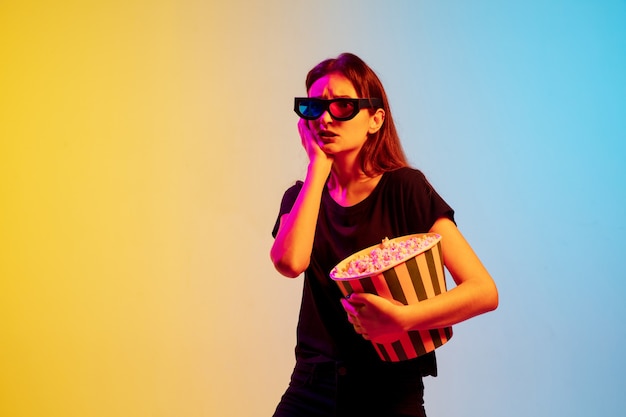 Young caucasian woman's portrait on gradient blue-yellow studio background in neon light