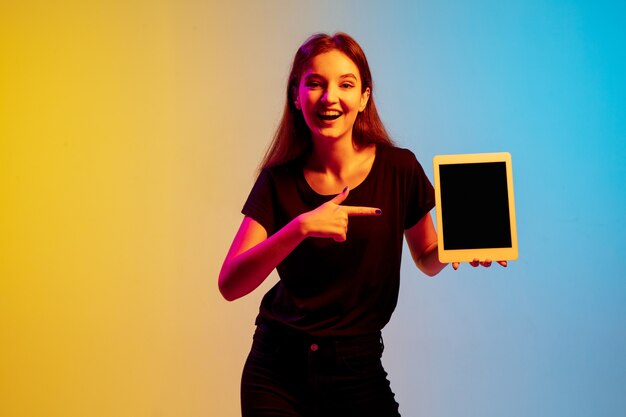 Young caucasian woman's portrait on gradient blue-yellow studio background in neon light