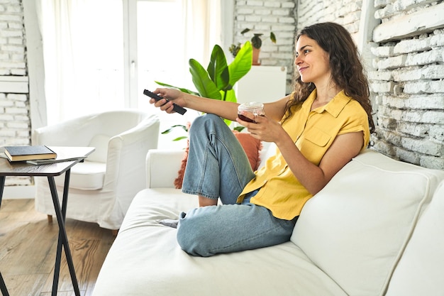 Photo a young caucasian woman seated on the sofa sipping tea and act