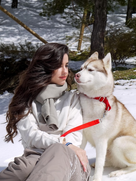 Young Caucasian woman seated with Siberian husky dog on the snow in the winter forest