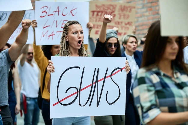 Giovane donna caucasica che grida mentre protestava contro l'uso delle armi con una folla di persone per le strade