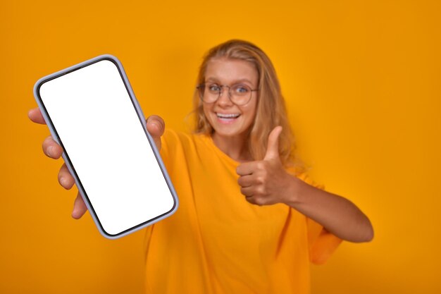 Young caucasian woman showing phone with white screen and thumbs up