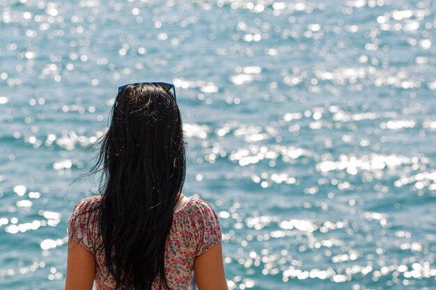 Young caucasian woman sits with her back on wooden bench overlooking blue sea