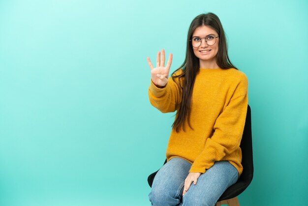 Young caucasian woman sitting on a chair isolated on blue background happy and counting four with fingers