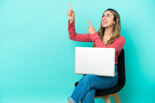 Young caucasian woman sitting on a chair with her pc isolated on blue background pointing with the index finger a great idea