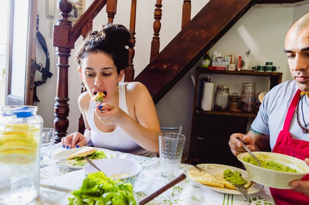 Young caucasian woman sitting at the dining table eating arepa