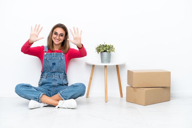 Young caucasian woman sitting on the floor among boxes counting ten with fingers