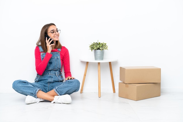 Young caucasian woman sitting on the floor among boxes keeping a conversation with the mobile phone with someone