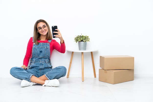 Young caucasian woman sitting on the floor among boxes making a selfie