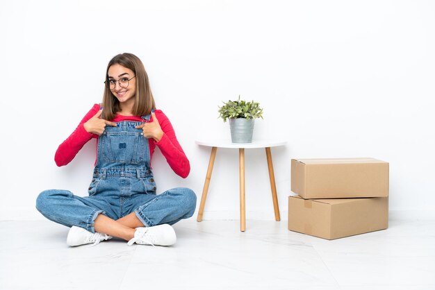 Young caucasian woman sitting on the floor among boxes with surprise facial expression