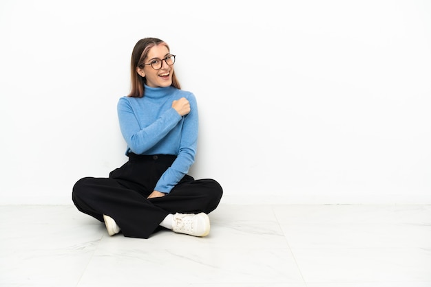 Photo young caucasian woman sitting on the floor celebrating a victory