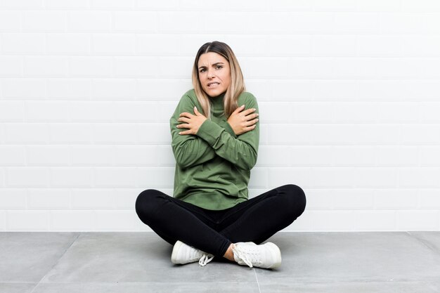 Young caucasian woman sitting on the floor going cold due to low temperature or a sickness.