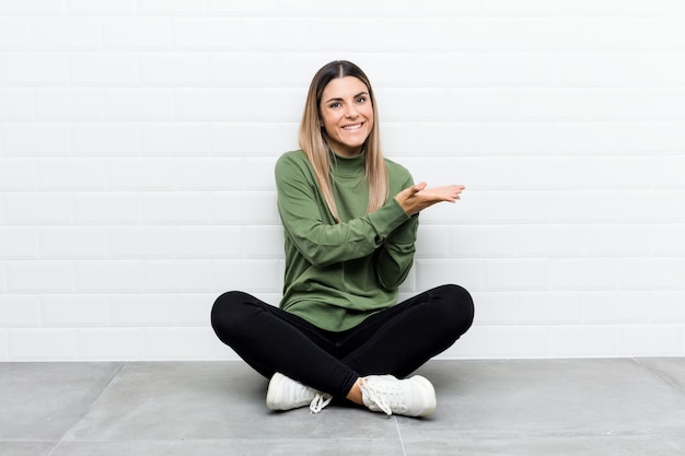 Young caucasian woman sitting on the floor holding a copy space on a palm.