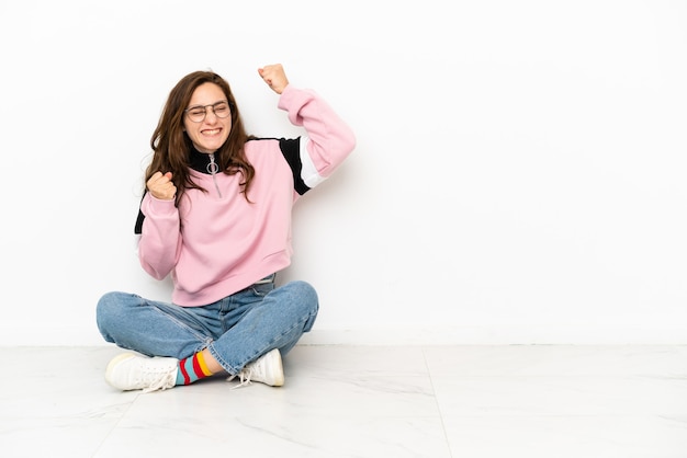 Young caucasian woman sitting on the floor isolated on white background celebrating a victory