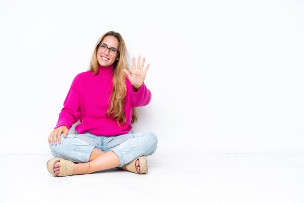 指で5を数える白い背景で隔離の床に座っている若い白人女性