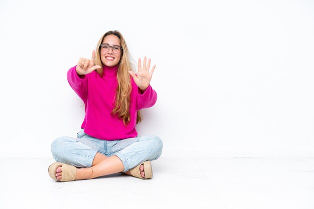 白い背景の上に座って指で7を数えている若い白人女性