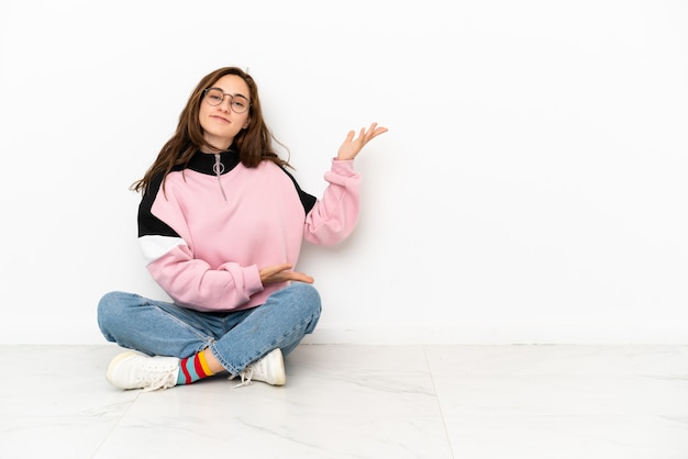 Young caucasian woman sitting on the floor isolated on white background extending hands to the side for inviting to come