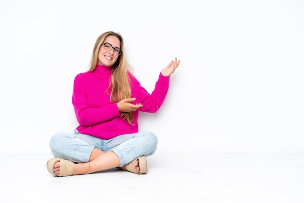 Young caucasian woman sitting on the floor isolated on white background extending hands to the side for inviting to come