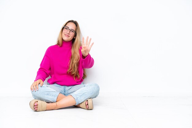 幸せな白い背景で隔離の床に座って、指で4を数える若い白人女性