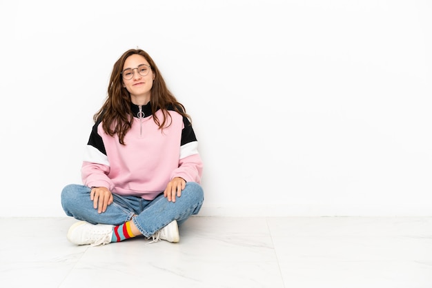 Young caucasian woman sitting on the floor isolated on white background laughing