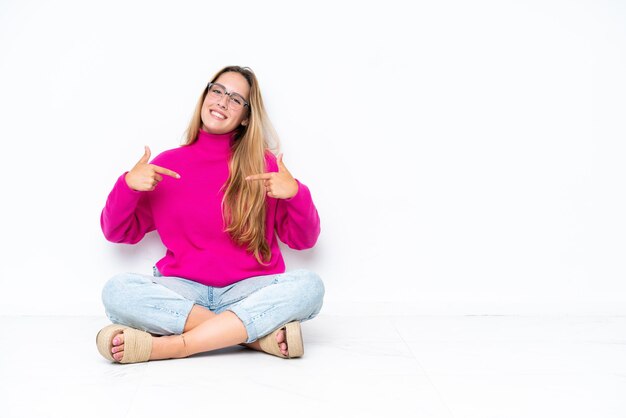 Photo young caucasian woman sitting on the floor isolated on white background proud and selfsatisfied