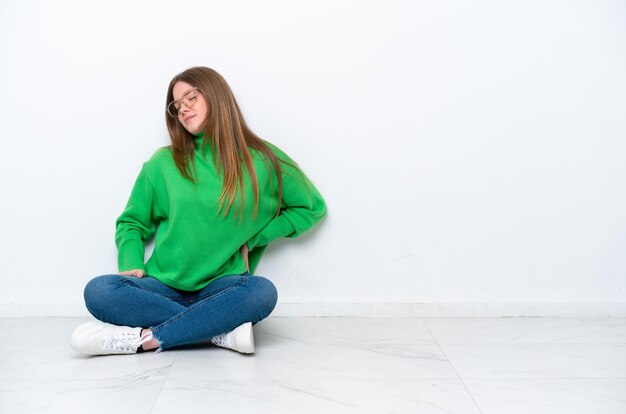 Young caucasian woman sitting on the floor isolated on white background suffering from backache for having made an effort