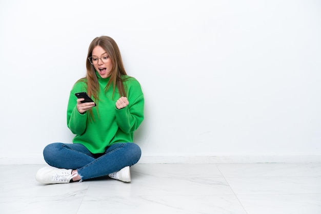 Young caucasian woman sitting on the floor isolated on white background surprised and sending a message