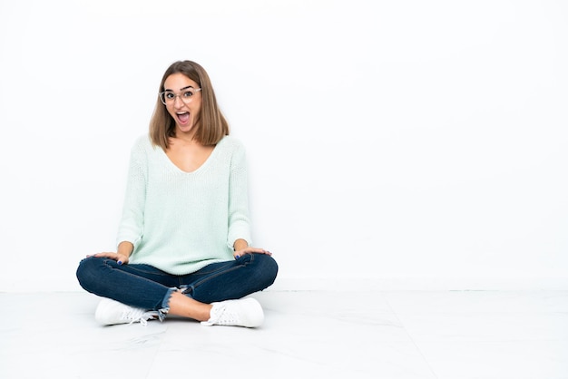 Photo young caucasian woman sitting on the floor isolated on white background with surprise facial expression