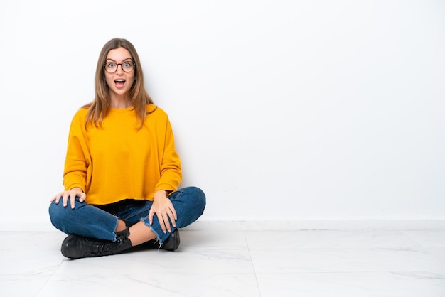 Young caucasian woman sitting on the floor isolated on white background with surprise facial expression