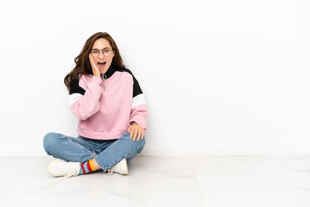 Photo young caucasian woman sitting on the floor isolated on white background with surprise and shocked facial expression