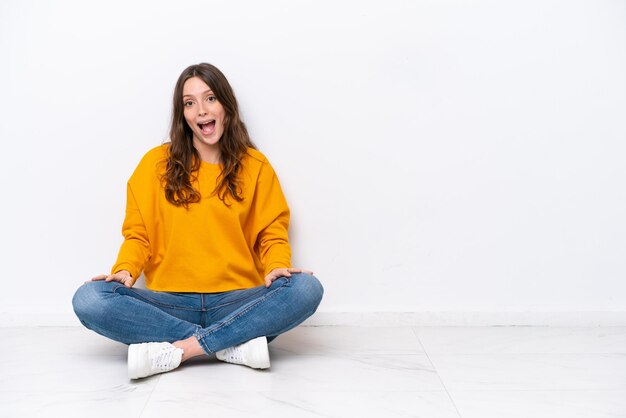 Young caucasian woman sitting on the floor isolated on white wall with surprise facial expression