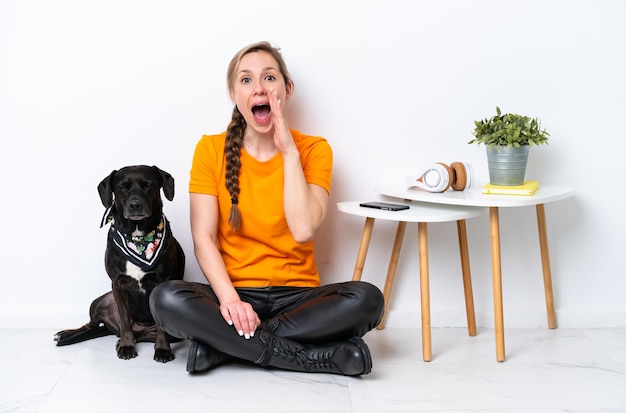 Young caucasian woman sitting on the floor with his puppy isolated on white background shouting with mouth wide open