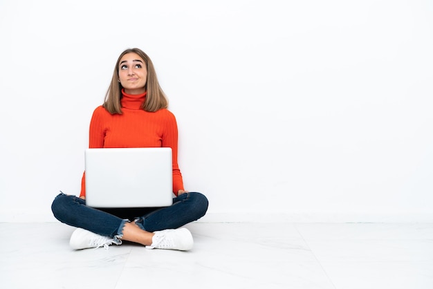 Young caucasian woman sitting on the floor with a laptop and looking up