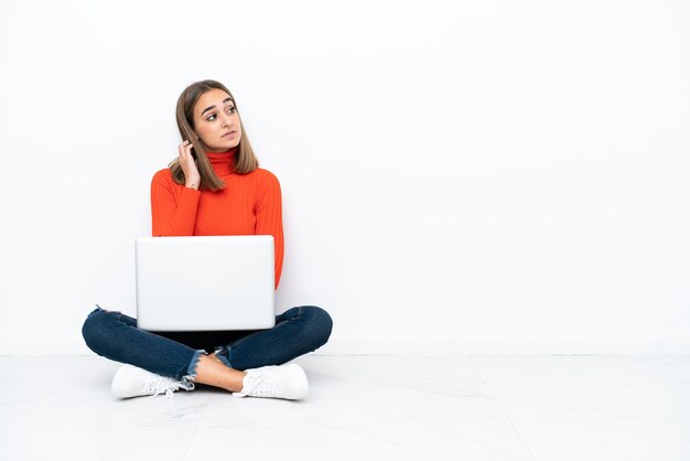 Young caucasian woman sitting on the floor with a laptop thinking an idea