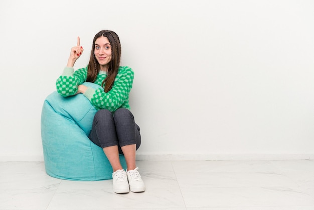 Young caucasian woman sitting on a puff isolated on white background