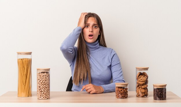 Young caucasian woman sitting at a table with food pot isolated on white background tired and very sleepy keeping hand on head.