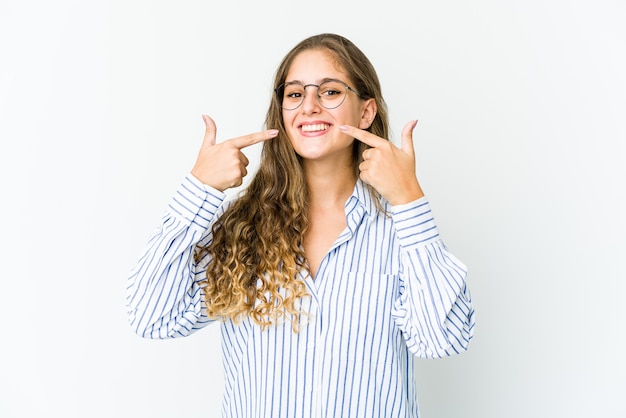 Young caucasian woman smiles, pointing fingers at mouth.