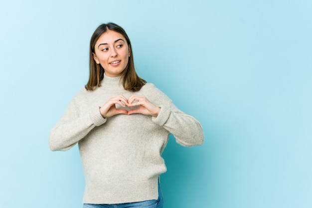 Young caucasian woman smiling and showing a heart shape with hands.