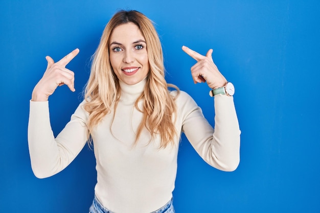 Young caucasian woman standing over blue background smiling pointing to head with both hands finger great idea or thought good memory