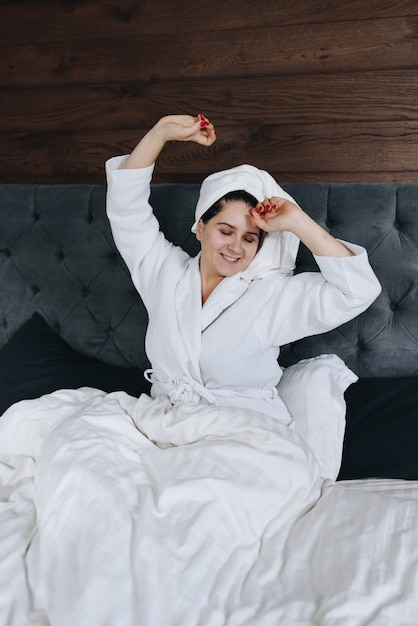 Young caucasian woman stretching in her bed in bedroom with towel on her head