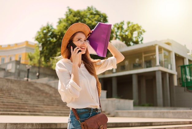 Young Caucasian woman student in casual clothing with esse in folder talking on phone going down the stairs