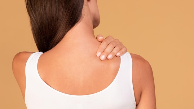 Young caucasian woman suffering from acute pain in her shoulder\
touching sore zone and massaging it panorama