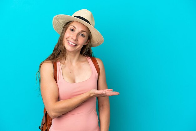 Young caucasian woman in summer holidays isolated on blue background presenting an idea while looking smiling towards