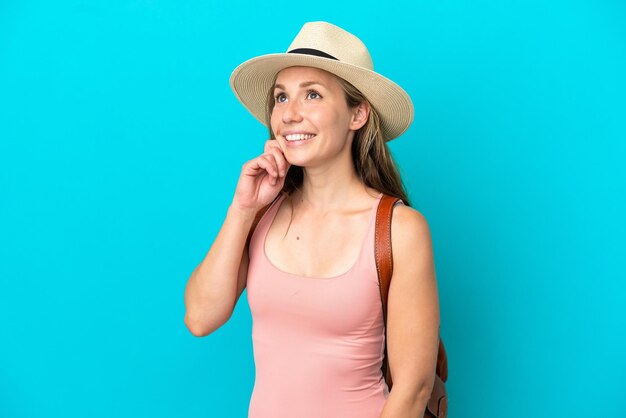 Young caucasian woman in summer holidays isolated on blue background thinking an idea while looking up