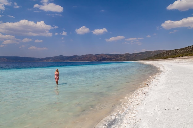 Young caucasian woman in the sunglasses and pink dress standing sexy posing in the lake salda turkey beautiful female happy relax walking on beach near sea with white sand and very clean blue water