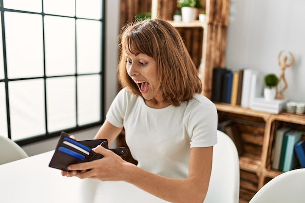 Young caucasian woman suprised looking wallet at home