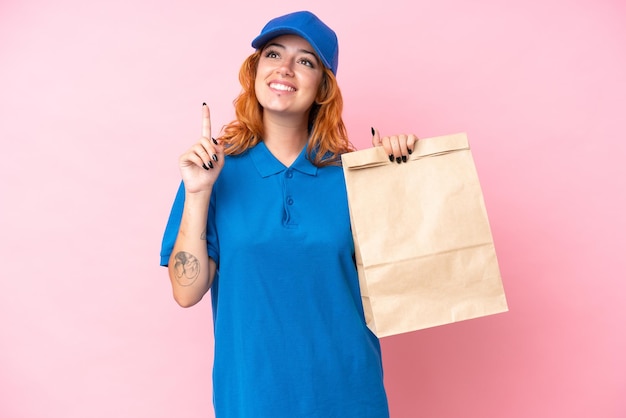 Young caucasian woman taking a bag of takeaway food isolated on pink background pointing up a great idea