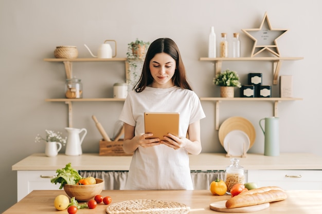 若い白人女性は、サラダを読むレシピを準備するキッチンでタブレットコンピューターを使用します