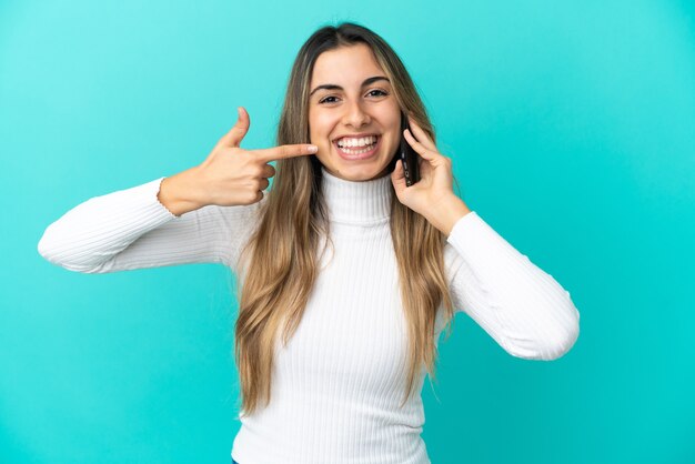 Giovane donna caucasica utilizzando il telefono cellulare isolato su sfondo blu, dando un pollice in alto gesto